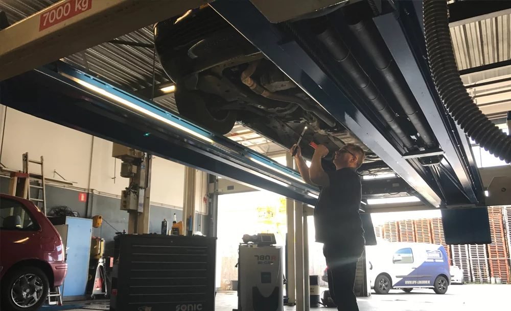 Monteur van APK Station Lanjouw voert een keuring uit onder een auto op de brug in de werkplaats